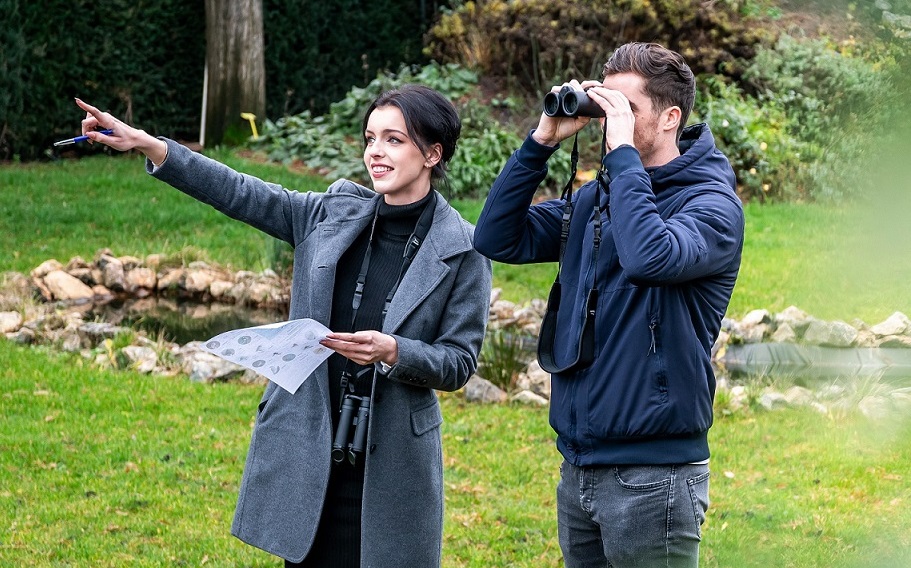 Two people meeting up for birdwatching. The man is looking through a binocular, while the woman points at something.